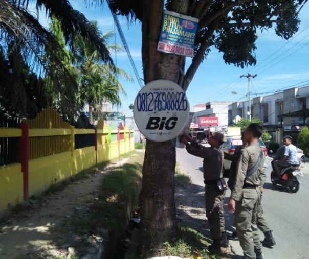 Petugas Satpol PP Pekanbaru menertibkan materi iklan ilegal dan dipasang di pohon pinggir jalan, Kamis (3/1/2019). Foto: Istimewa.