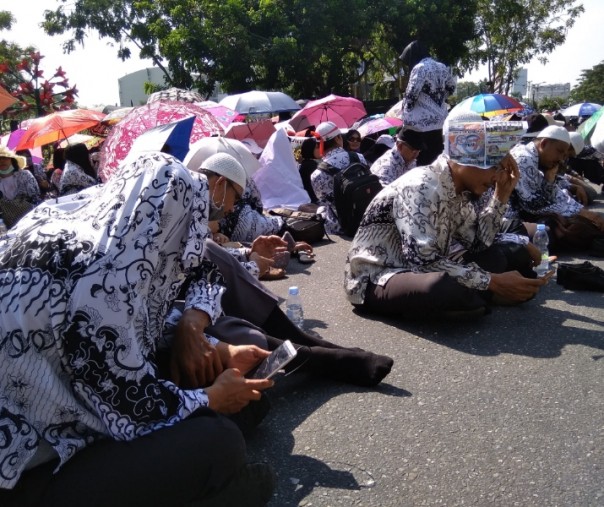 Beberapa orang guru laki-laki menutupi badannya dengan baju dan kertas koran saat aksi unjuk rasa di depan kantor wali kota Pekanbaru, Jumat (22/3/2019). Foto: Surya/Riau1.