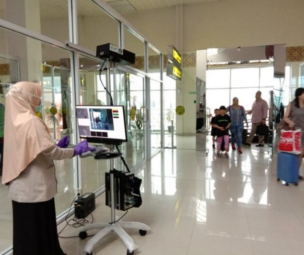Dokter dari Kantor Kesehatan Pelabuhan saat memantau panas tubuh penumpang yang tiba di terminal kedatangan internasional Bandara SSK II Pekanbaru. Foto: Istimewa.