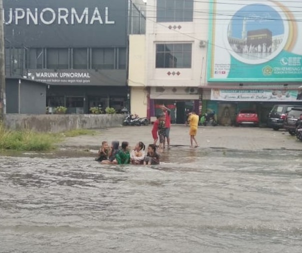 Bocah-bocah bermain di tengah banjir di Jalan Soebrantas Panam, Selasa (18/6/2019). Foto: Riau1.