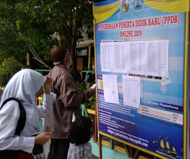 Orang tua bersama anaknya saat melihat papan pengumuman anak yang diterima di SMPN 5 Pekanbaru, Jumat (5/7/2019). Foto: Surya/Riau1.
