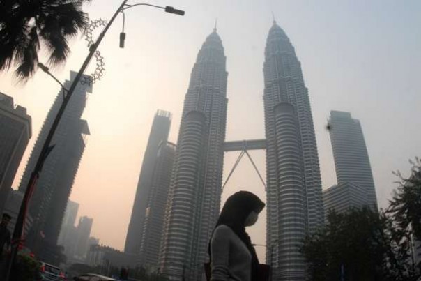 Seseorang menggunakan masker lewat depan Menara Kembar Patronase Diselimuti kabut asap tebal, Selasa.