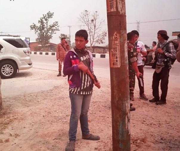 Aksi kocak bocah di Kampar sambut kedatangan Jokowi, bergaya bak prajurit sembari menenteng senjata laras panjang mainan dan berdiri di antara aparat yang ditugasi mengamankan tempat kedatangan Presiden RI di Desa Rimbo Panjang, Kampar.