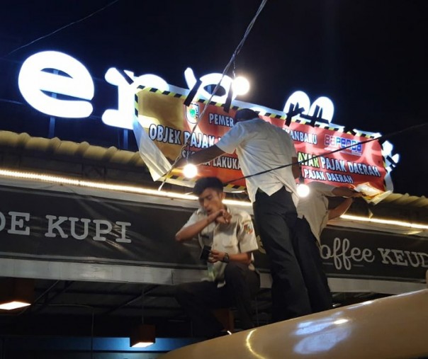 Petugas Bapenda Pekanbaru memasang spanduk tagihan pajak di Er Cafe di Jalan Arifin Ahmad, Selasa (22/10/2019). Foto: Istimewa.