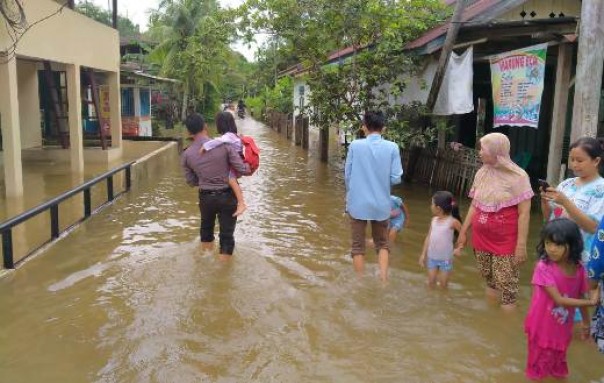 Salah seorang aparat Polsek Kuantan Mudik membantu seorang anak melintasi banjir