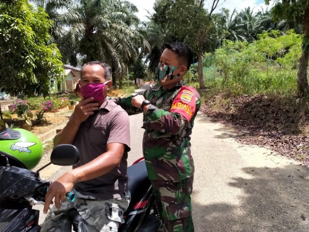 Sertu Siswanto saat membagikan masker sekaligus memasangkan langsung kepada warga Pelita, Rabu (29/04)/Net