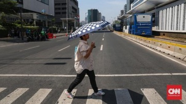 Seorang pejalan kaki pakai payung karena panas terik. 