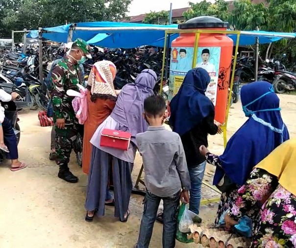 Babinsa Kerumutan Kopda Roni Pasla meminta ibu-ibu mencuci tangan sebelum masuk ke Pasar Induk Bukit Garam, Minggu (31/5/2020). Foto: Istimewa.