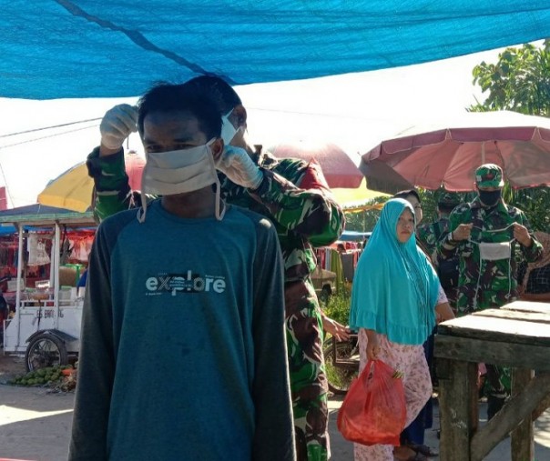Anggota Koramil 14 Kepenuhan memasangkan masker ke salah seorang pedagang Pasar Kamis Rokan Hulu, Minggu (7/6/2020). Foto: Istimewa.