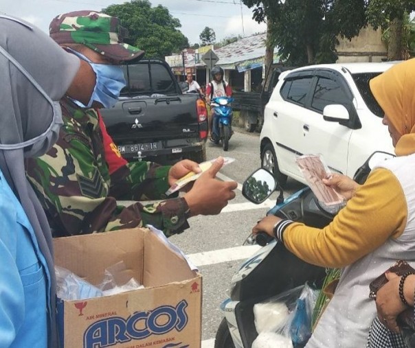 Babinsa Bangkinang Serka Sugeng Waluyo bersama mahasiswi UNRI membagikan masker di persimpangan Jalan Desa Ridanpermai, Minggu (14/6/2020). Foto: Istimewa.