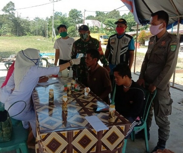 Babinsa Koramil 13 Rokan Kopda Febrianto mendampingi petugas kesehatan saat mengecek suhu tubuh warga di pos pemeriksaan, Jumat (3/7/2020). Foto: Istimewa.