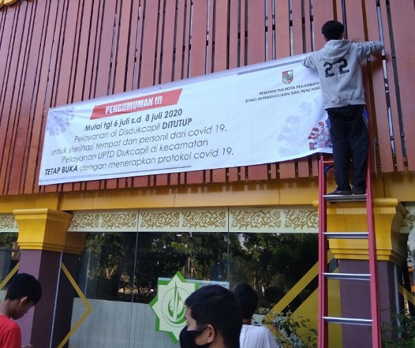 Para pekerja sedang memasang spanduk pemberitahuan penutupan Kantor Disdukcapil Pekanbaru, Minggu (5/7/2020). Foto: Surya/Riau1.