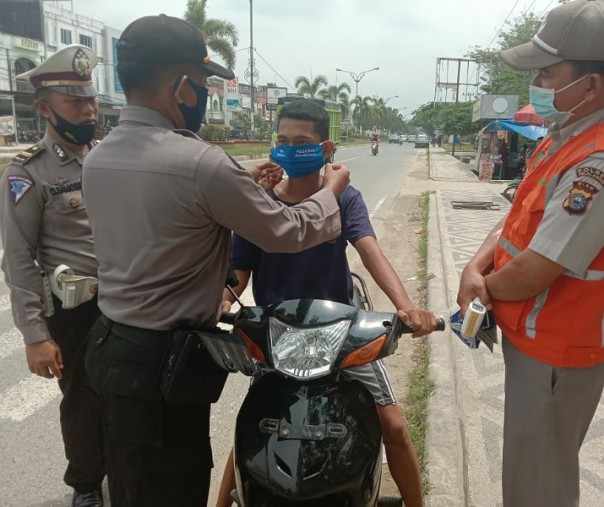 Personel Polres Pelalawan saat memasangkan masker kepada pengendara pelanggar dalam Operasi Patuh Lancang Kuning, Rabu (29/7/2020). Foto: Istimewa.