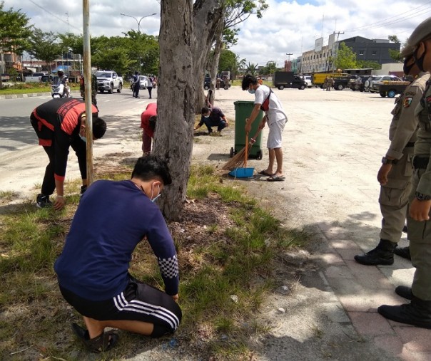 Warga yang tak mengenakan masker saat menjalani hukuman mencabut rumput di pinggir Jalan Soekarno-Hatta Pekanbaru, beberapa waktu lalu. Foto: Surya/Riau1.