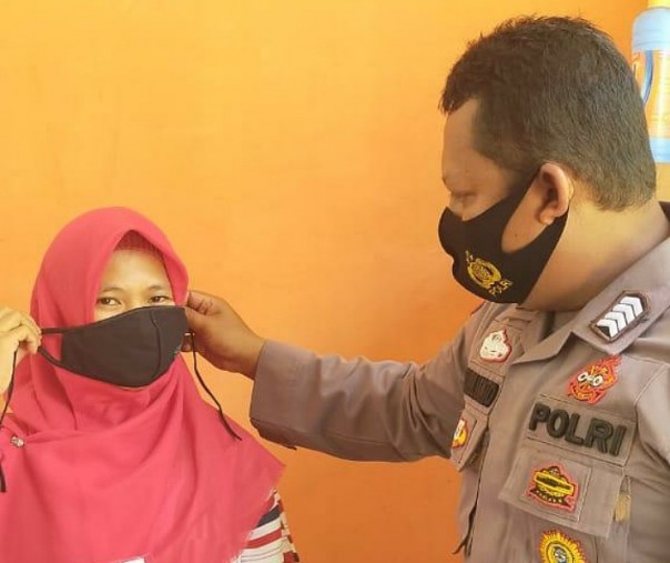 Bhabinkamtibmas Polsek Pangkalan Kerinci Bripka Tri Yulianto saat memasangkan masker ke seorang warga Desa Mekar Jaya, Kamis (17/9/2020). Foto: Istimewa.