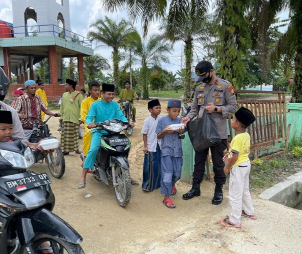 Kapolsek Langgam Ipda M Fadlillah membagikan nasi kotak ke anak-anak dan jemaah Masjid Al Muhajirin di Desa Tambak, Jumat (4/12/2020). Foto: Istimewa. 