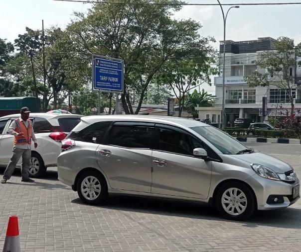 Seorang juru parkir mengarahkan mobil keluar dari area parkir sebuah toko di Jalan Arifin Ahmad. Foto: Surya/Riau1.