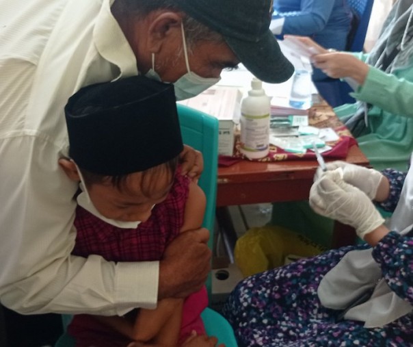 Murid MI Al Ikhwan dipegang orang tuanya saat akan disuntik vaksin, Jumat (28/1/2022). Foto: Surya/Riau1. 