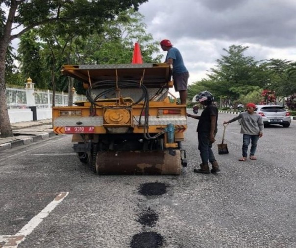 Pekerja Dinas PUPR Pekanbaru menambal berlubang di samping kantor gubernur Riau. Foto: Istimewa. 